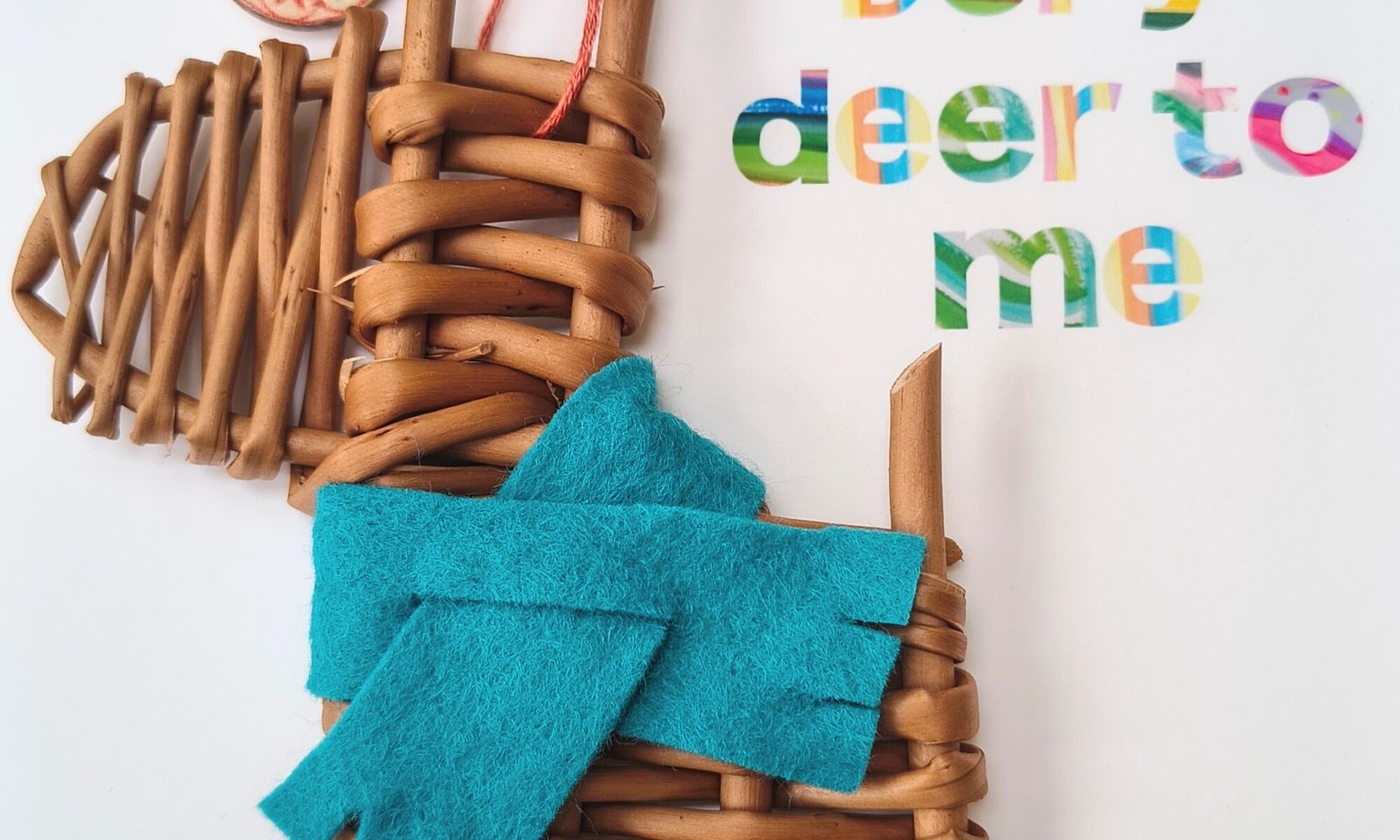 a small deer made from orange / brown willow with a teal scarf on a white card with colourful writing saying You are Deer to Me